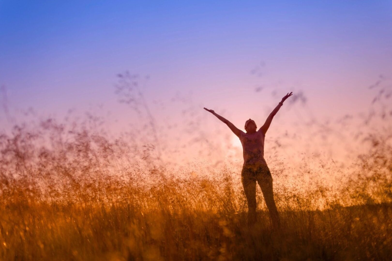 A person standing in the grass with their arms raised.