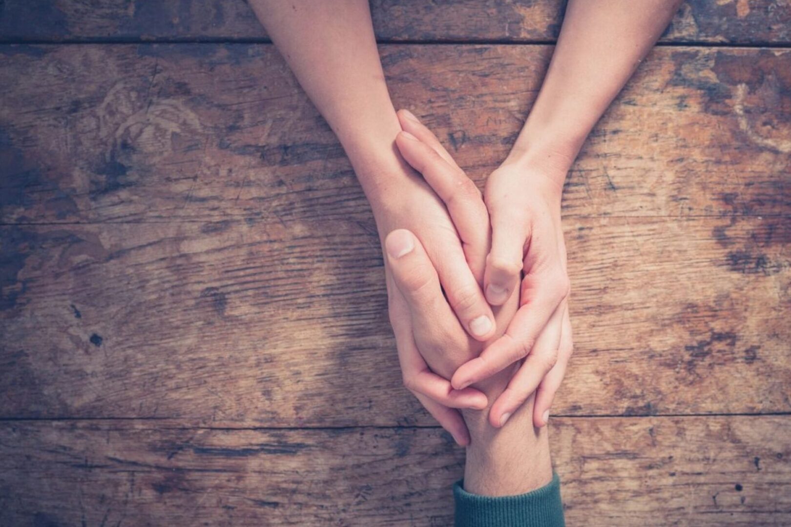 Two people holding hands on a wooden table.