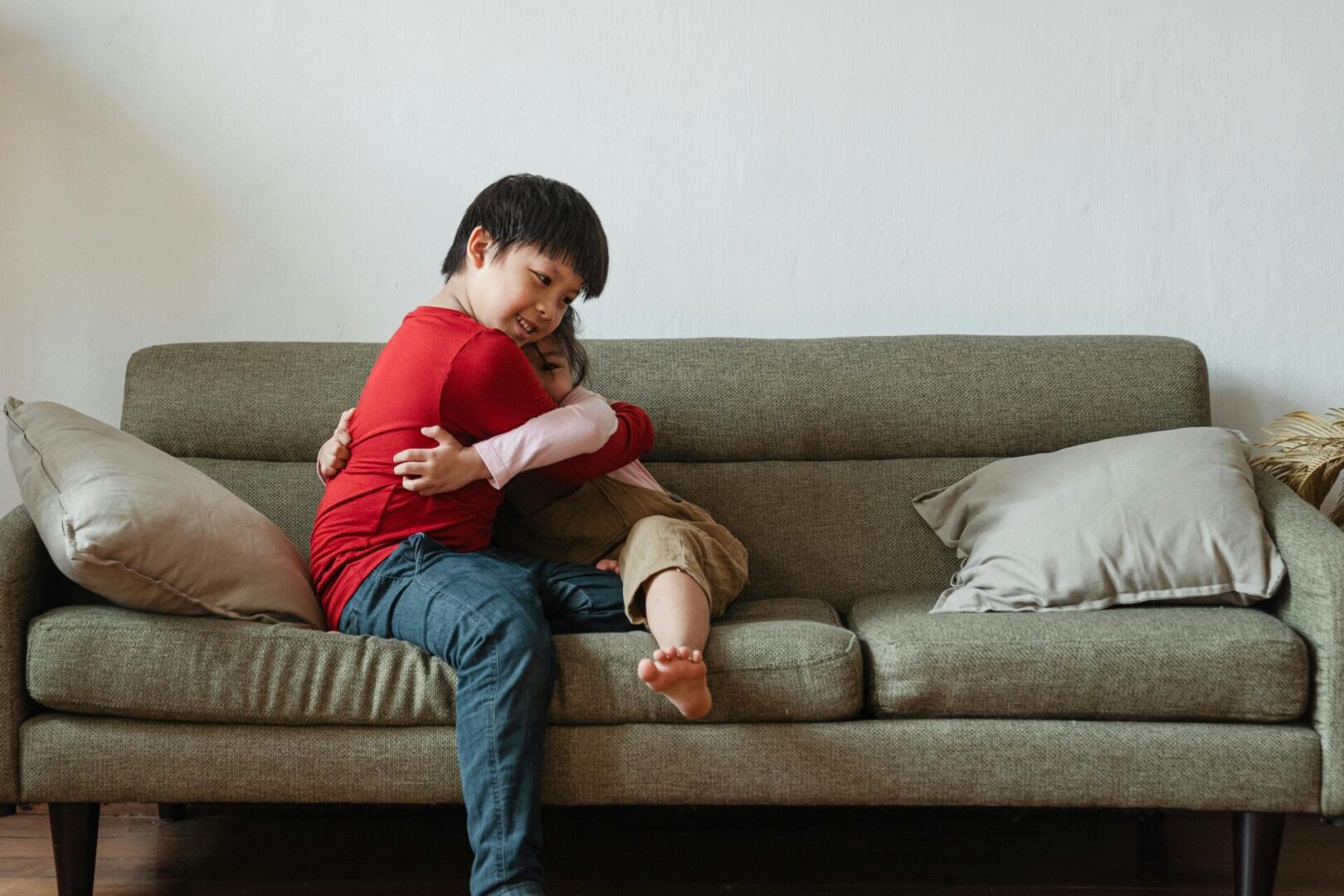 A boy sitting on the couch with his arm around another boy.